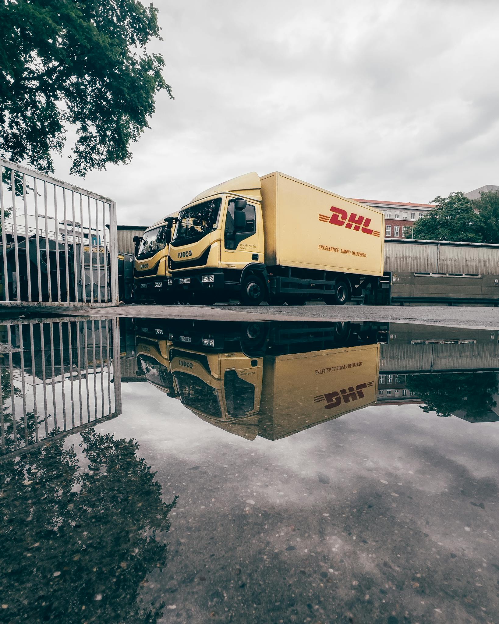 Yellow DHL trucks reflecting in a puddle on a cloudy day in Berlin, Germany.